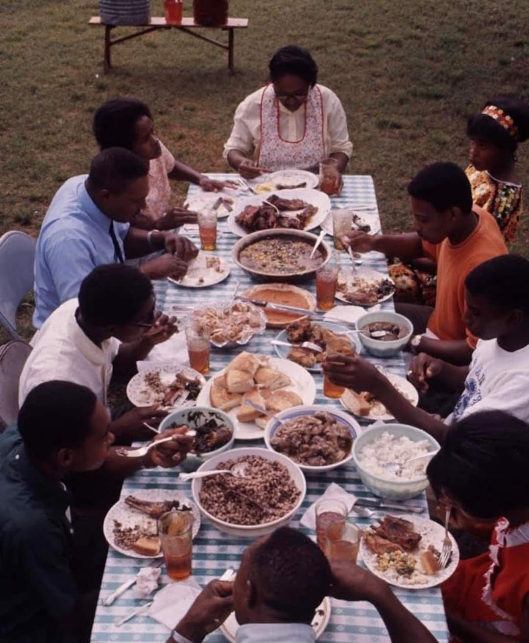 An extended family sharing a meal outdoors at a long table