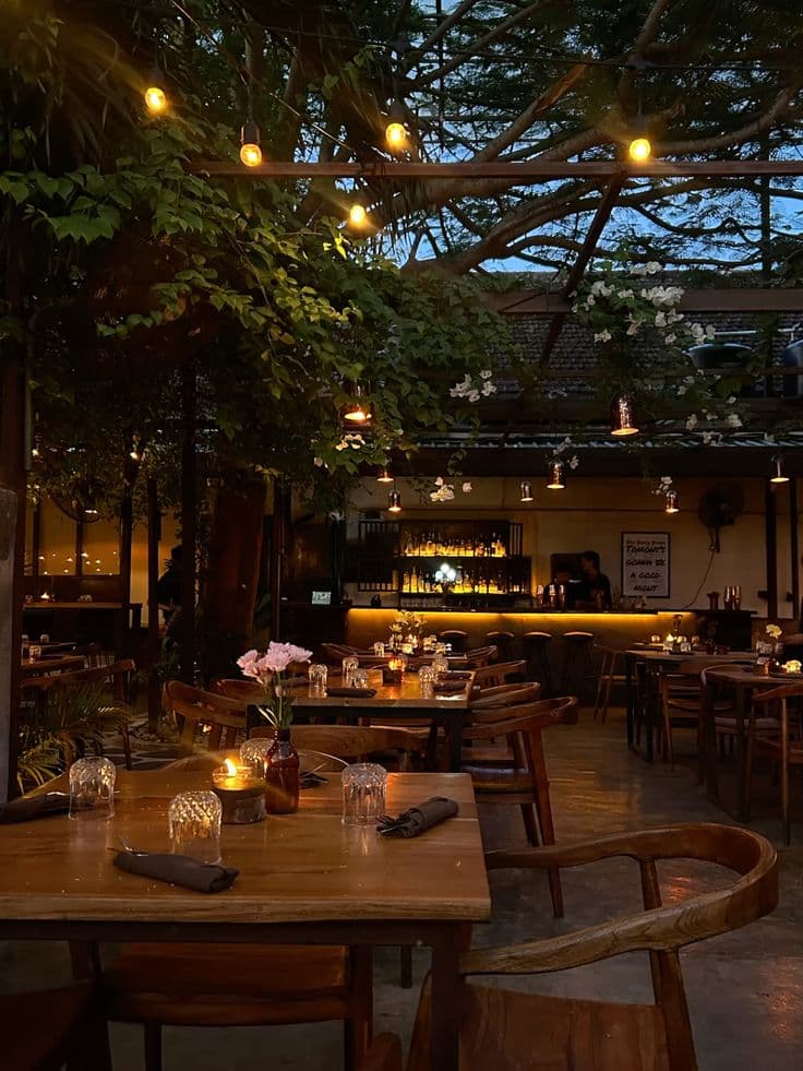 Warmly lit interior with timber tables under string lights and greenery